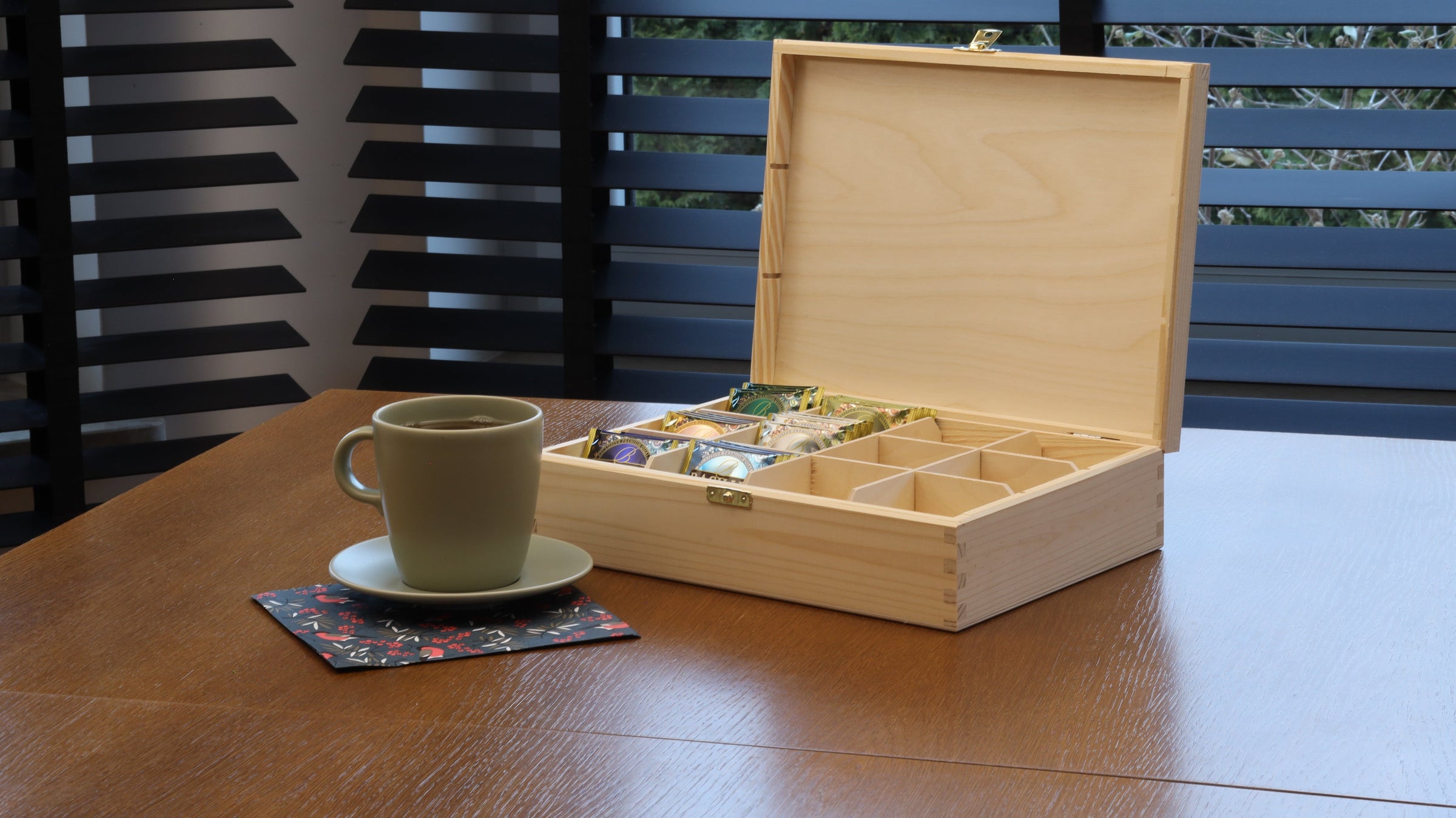 Natural wooden tea bag box with selection of tea bags presented on table next to tea cup